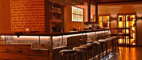 A bar area with a long counter, stools, and shelves with bottles.