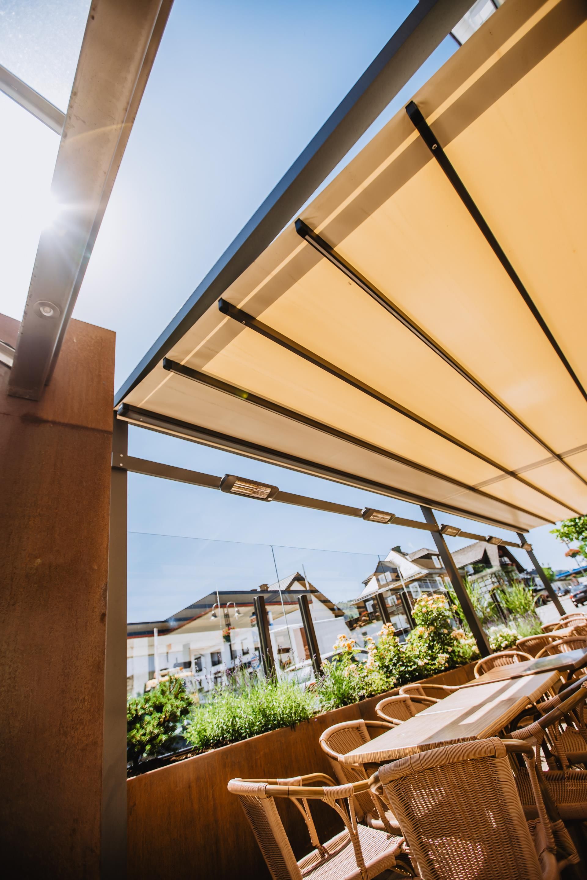 An outdoor seating area with a table and chairs, a pergola overhead, and a view of buildings in the background.