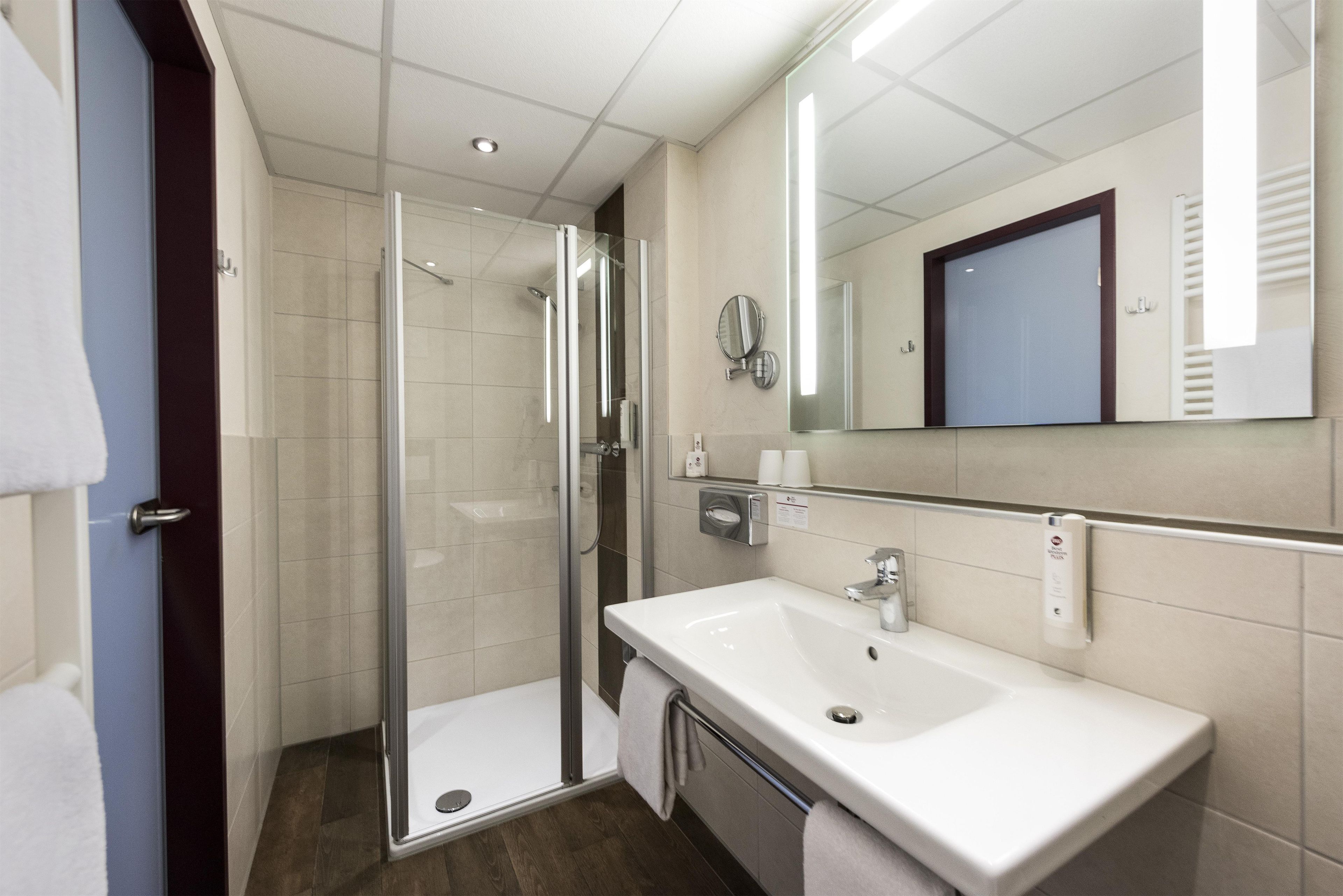 A modern bathroom with a glass shower enclosure, a white sink, and a large mirror.
