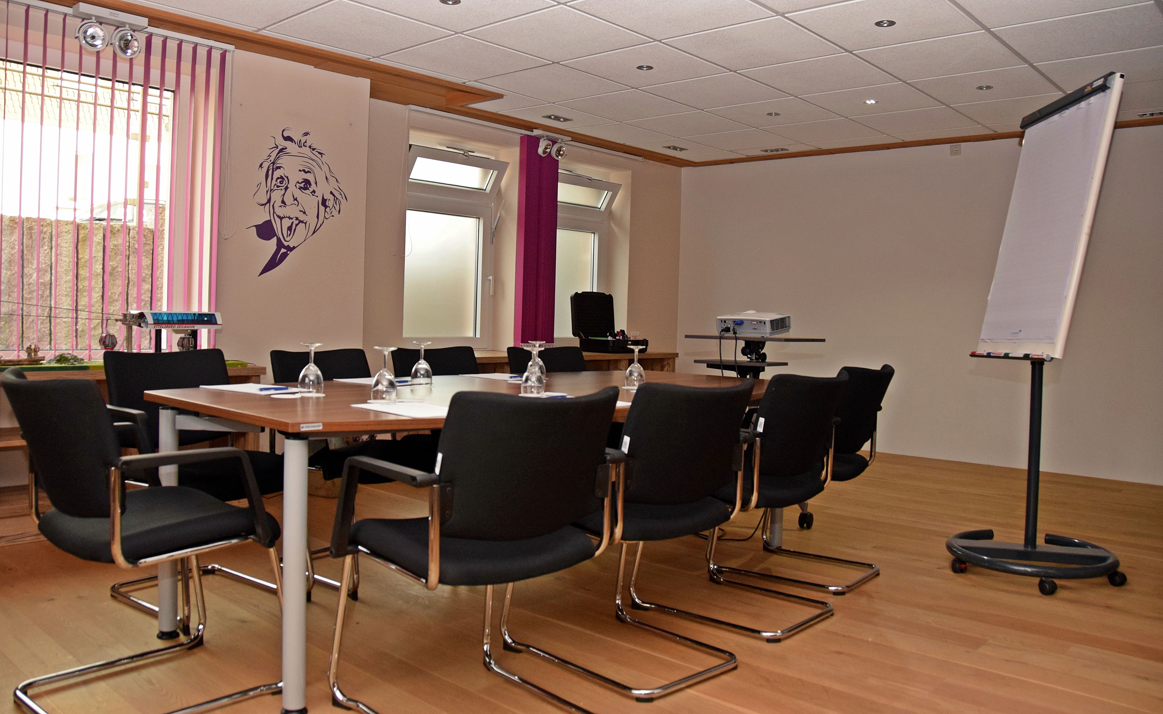 A conference room with a large table, black chairs, a whiteboard, and a projector.