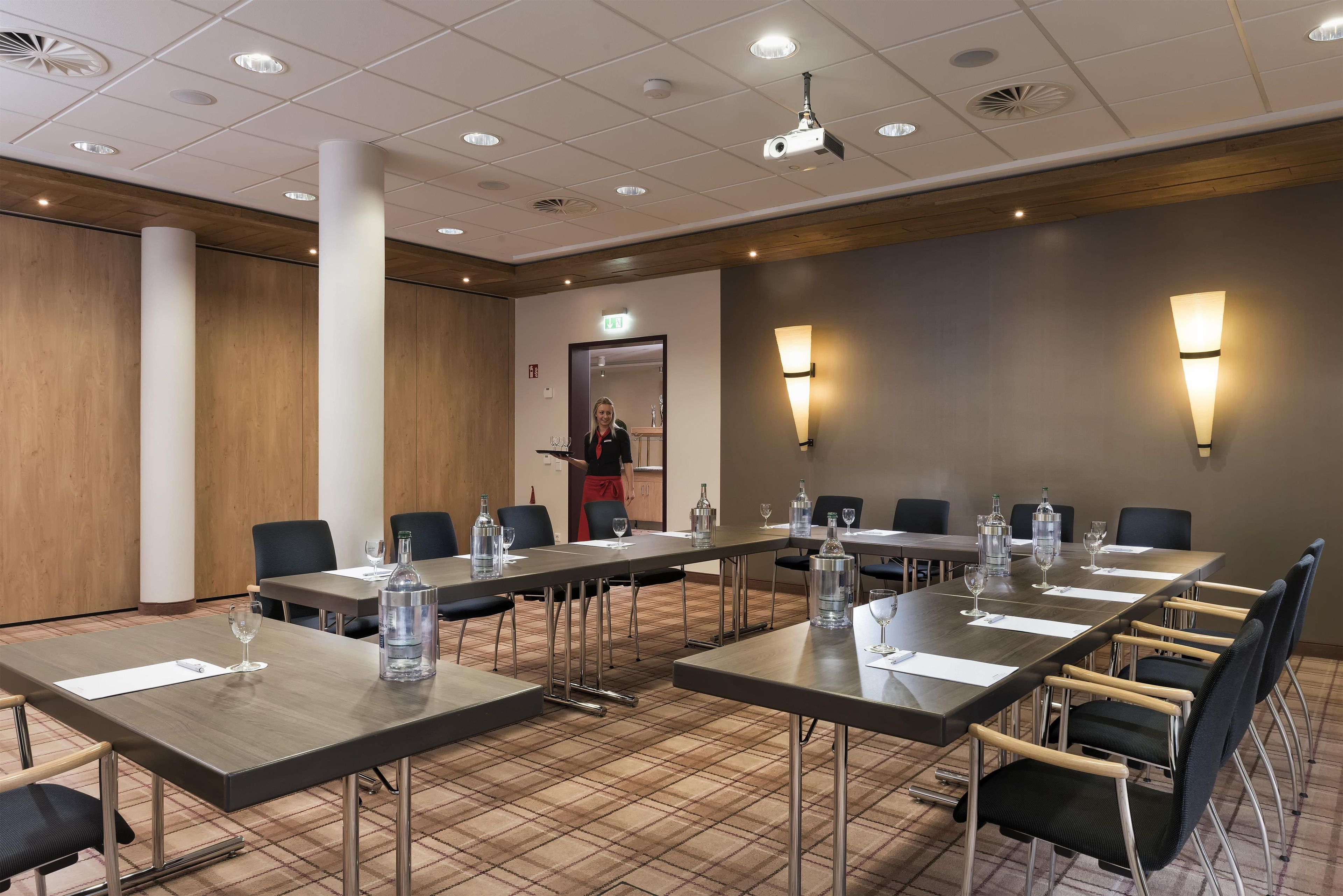 A conference room with long tables, chairs, and a person standing near the door.