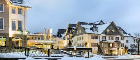 Un hotel de varios pisos, suelo cubierto de nieve y un puente en primer plano.