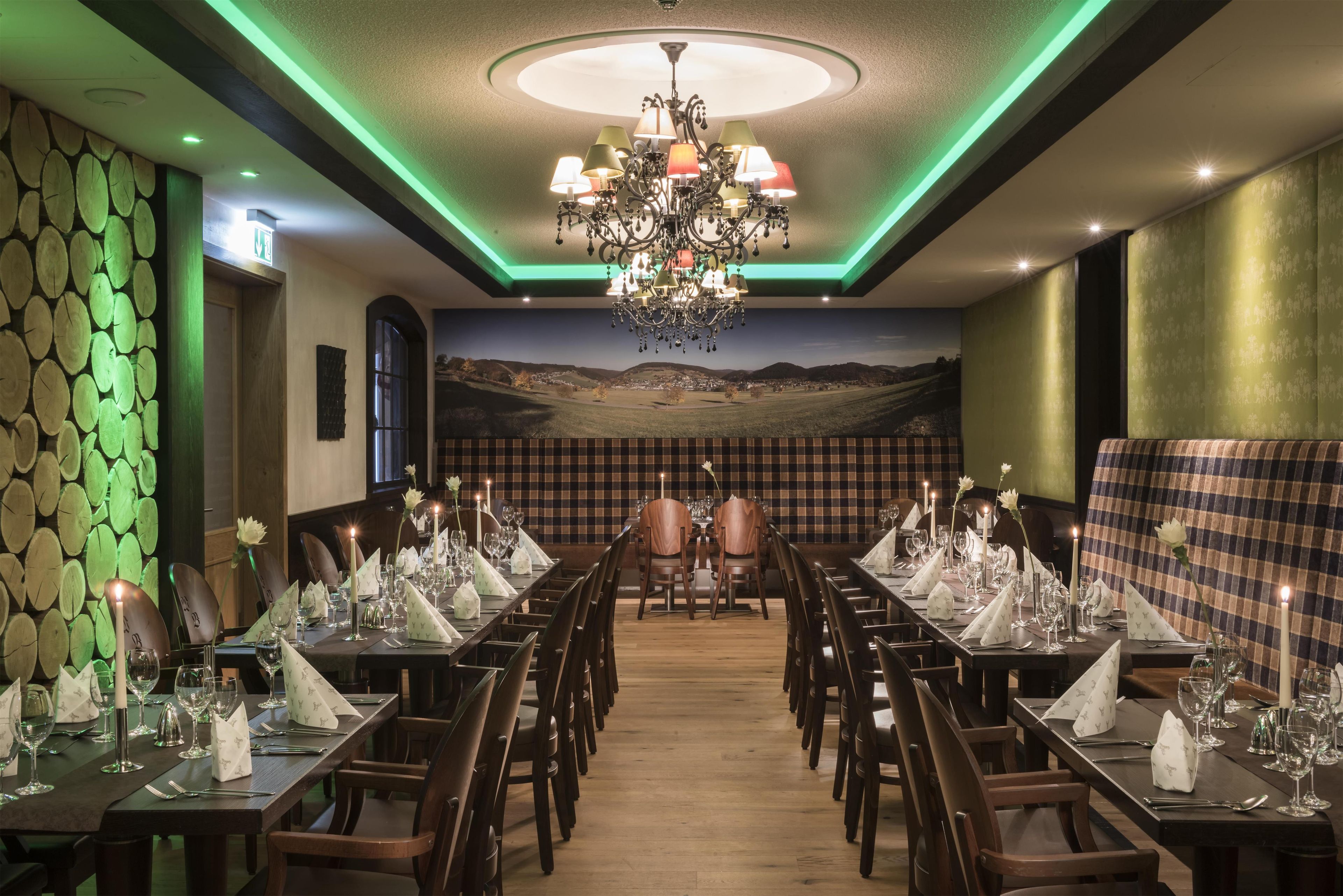 Ein Restaurant mit einem langen Esstisch, Stühlen und einer Kristallleuchter. Eine Wand zeigt ein Schachbrettmuster und ein Landschaftsgemälde.