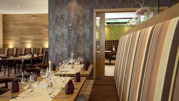 A restaurant with a long dining table set for a meal, wooden walls, and a striped sofa.