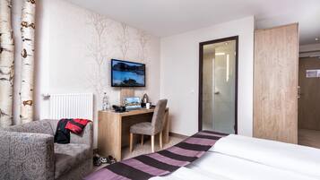 Ein Hotelzimmer mit einem Bett, einem Schreibtisch mit Computer, einem Stuhl, einem an der Wand befestigten Fernseher und einem Fenster.