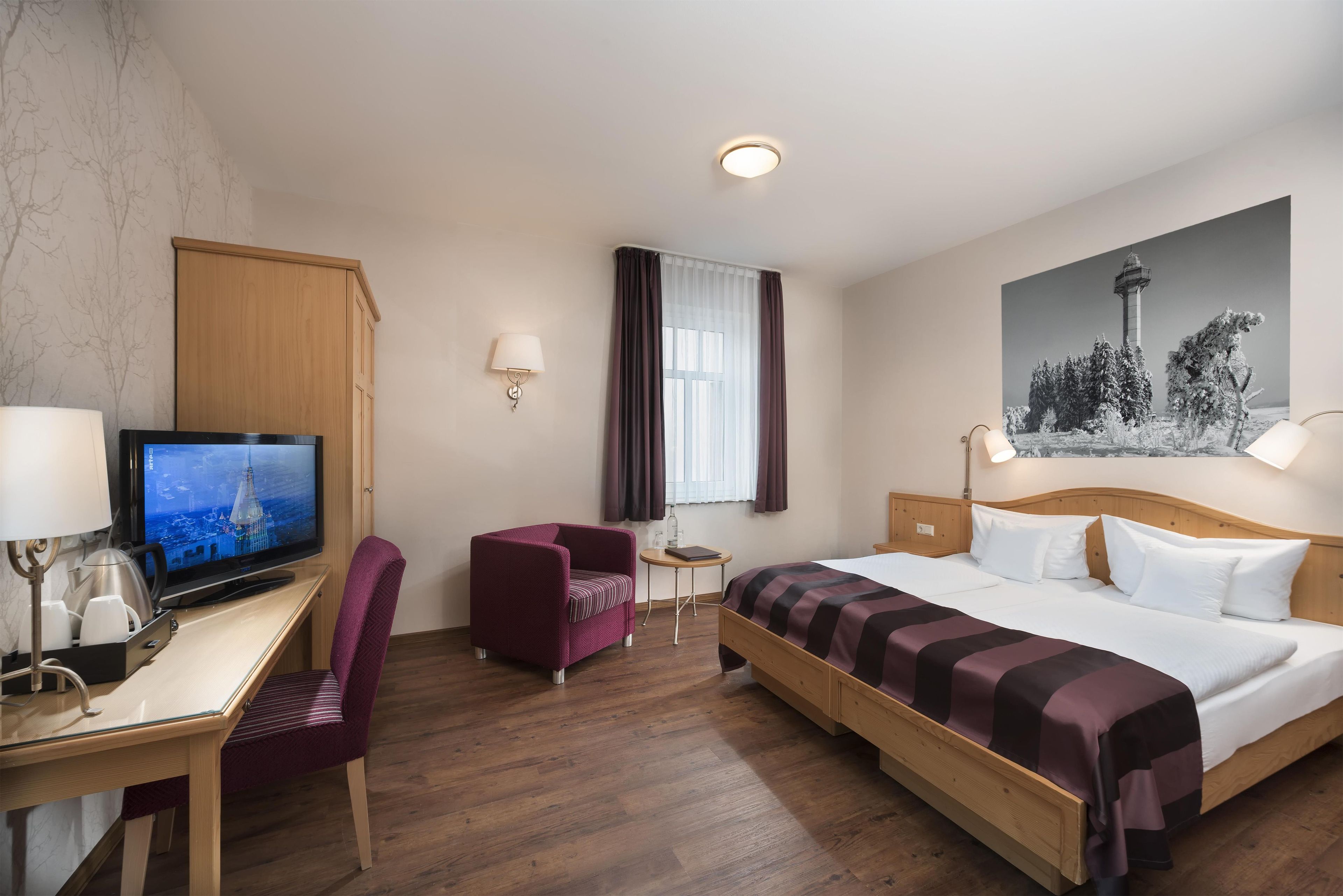 Una habitación de hotel con cama, escritorio, silla, televisión y un cuadro en la pared.