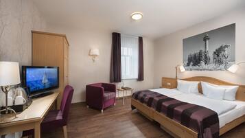 Una habitación de hotel con cama, escritorio, silla, televisión y un cuadro en la pared.