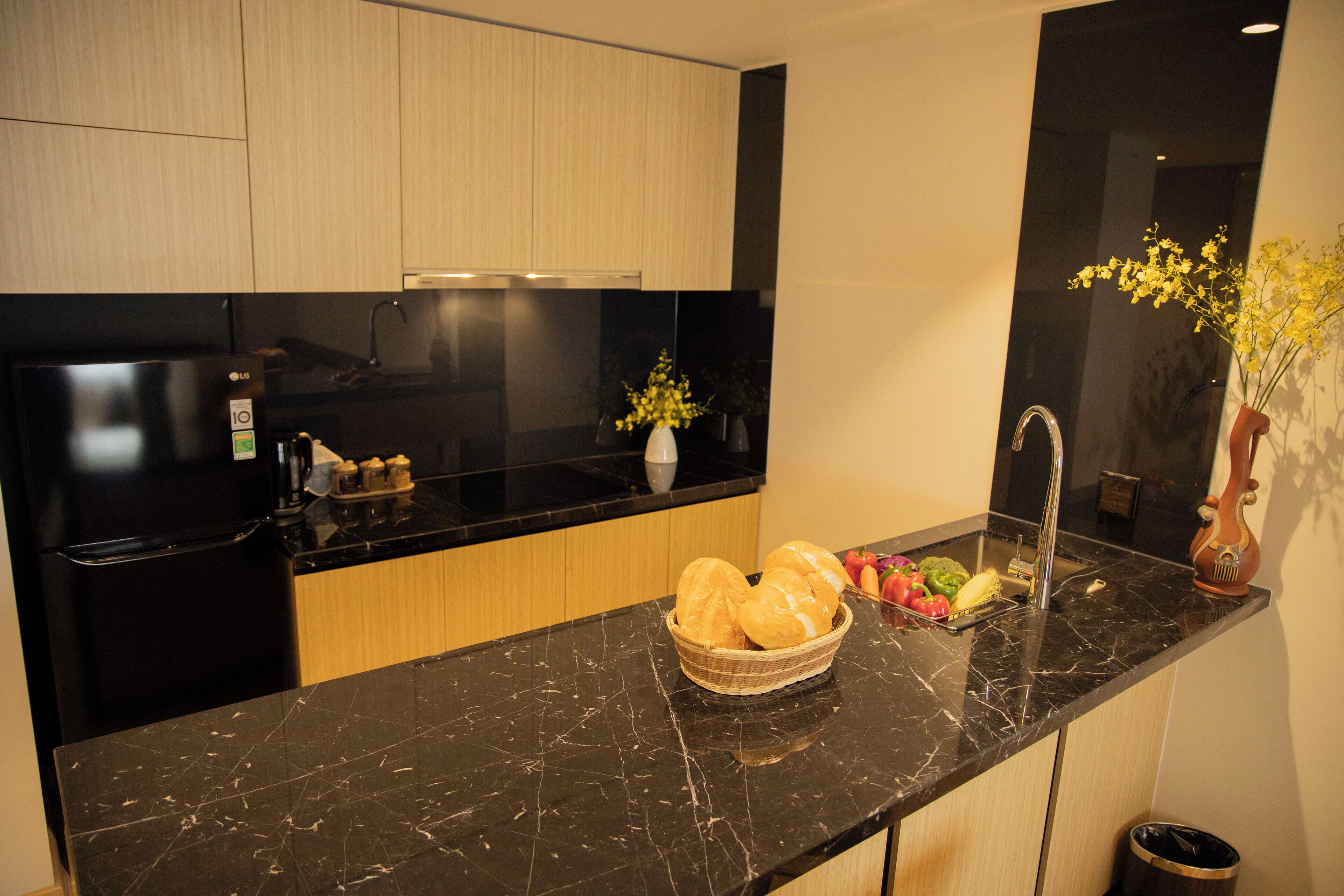 A modern kitchen with a black marble countertop, a black refrigerator, wooden cabinets, a sink, and a vase with flowers.