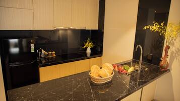 A modern kitchen with a black marble countertop, a black refrigerator, wooden cabinets, a sink, and a vase with flowers.
