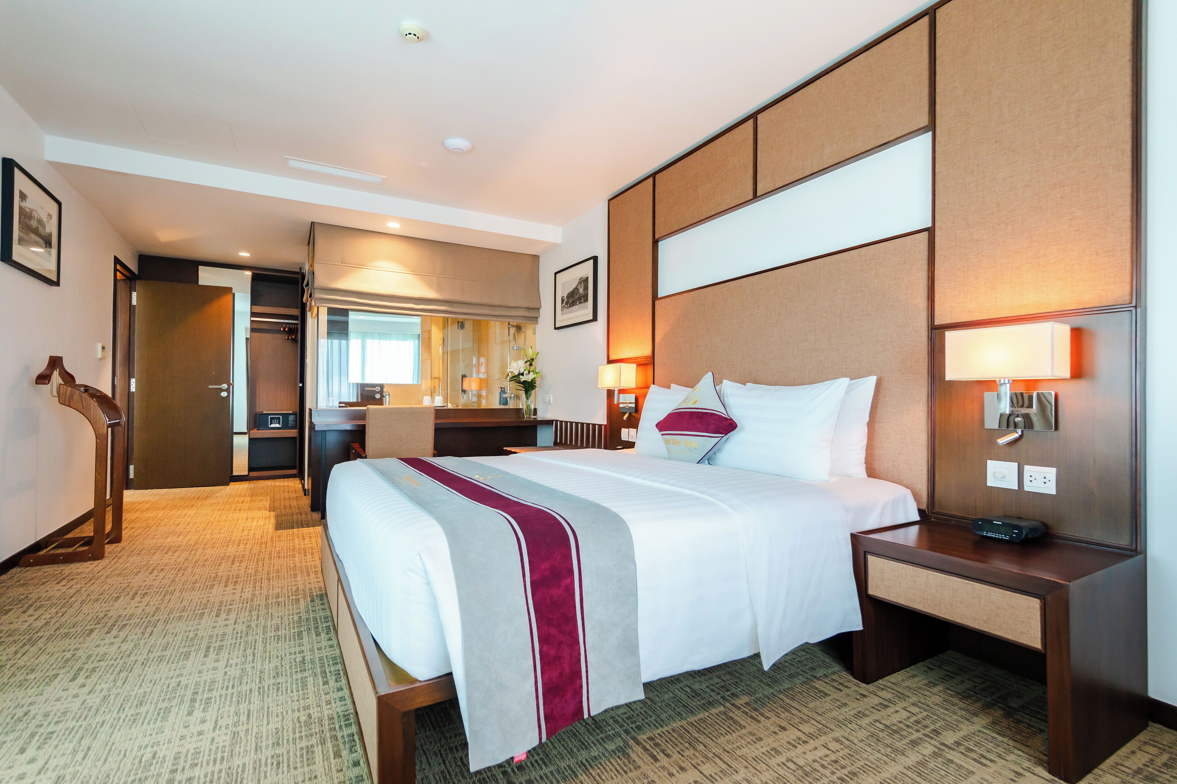 A hotel room with a large bed, bedside tables, a desk, and a bathroom visible through an open door.