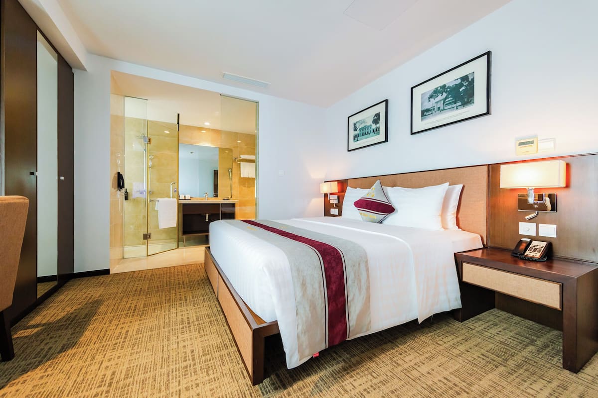 A hotel room with a bed, bedside tables, a nightstand, a mirror, and a door leading to a bathroom.