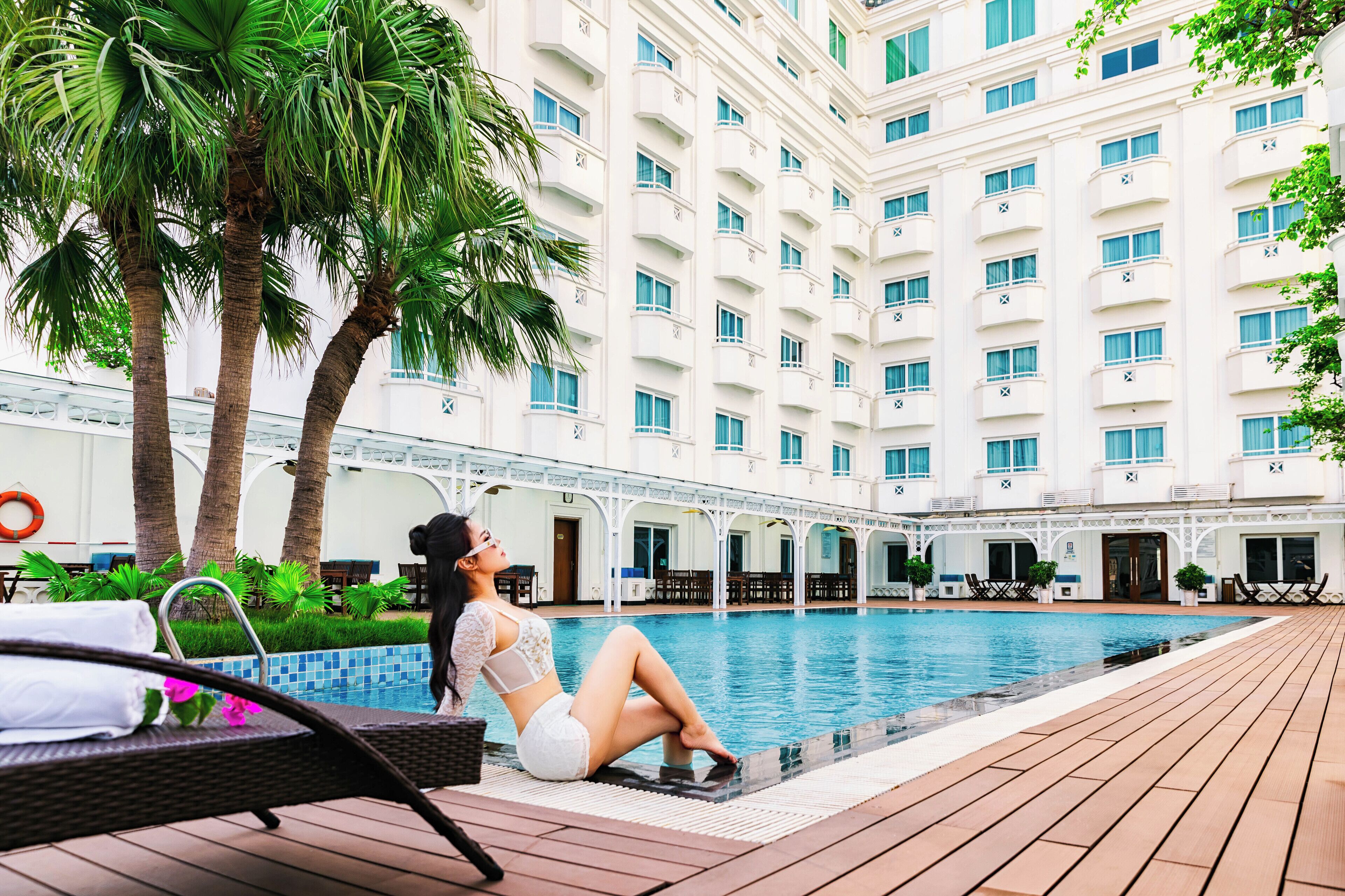 A poolside area with a lounge chair, palm trees, and a building with multiple balconies.