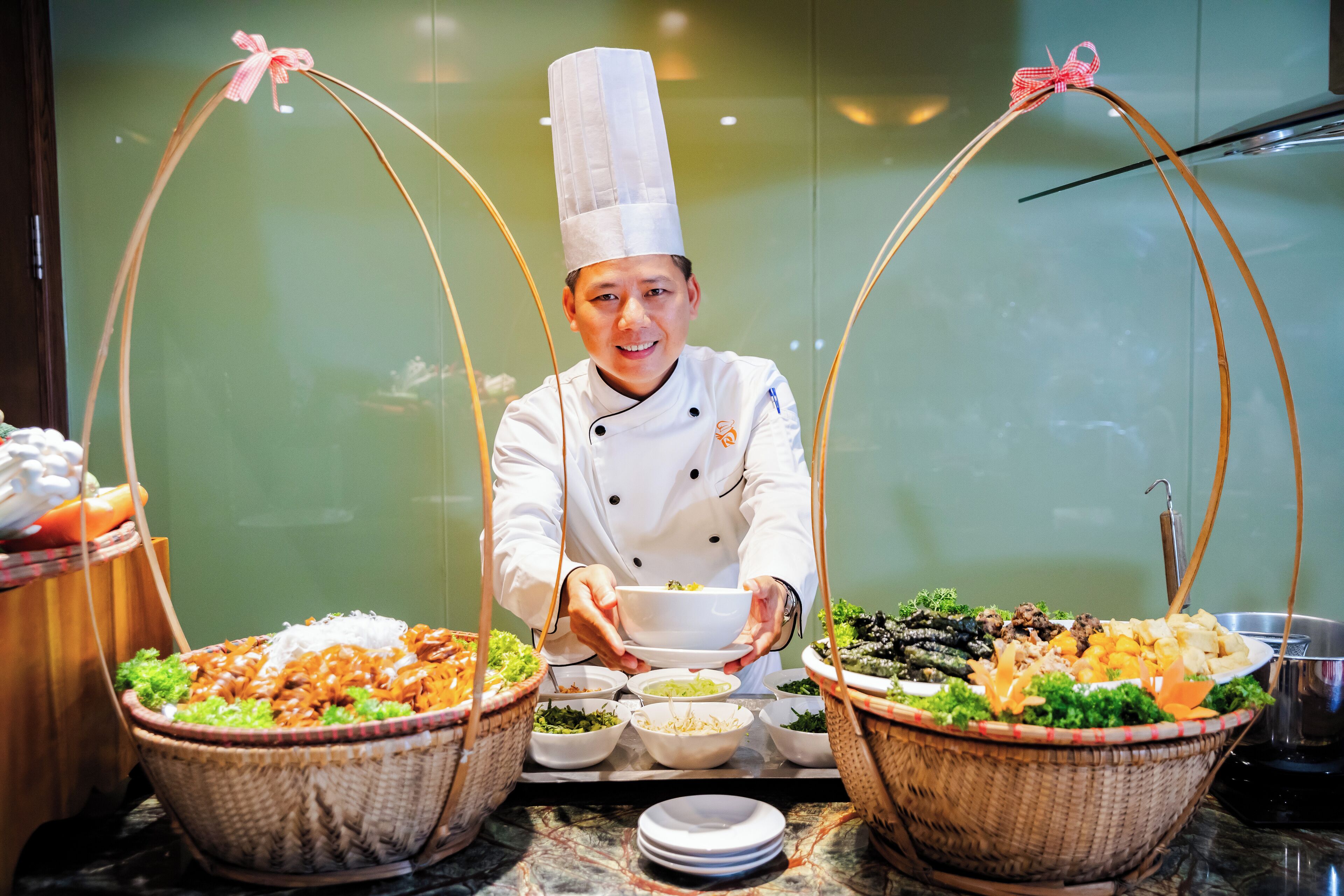 Un chef, vêtu d’un uniforme blanc et coiffé d’un haut chapeau, présente deux grands paniers remplis de nourriture.