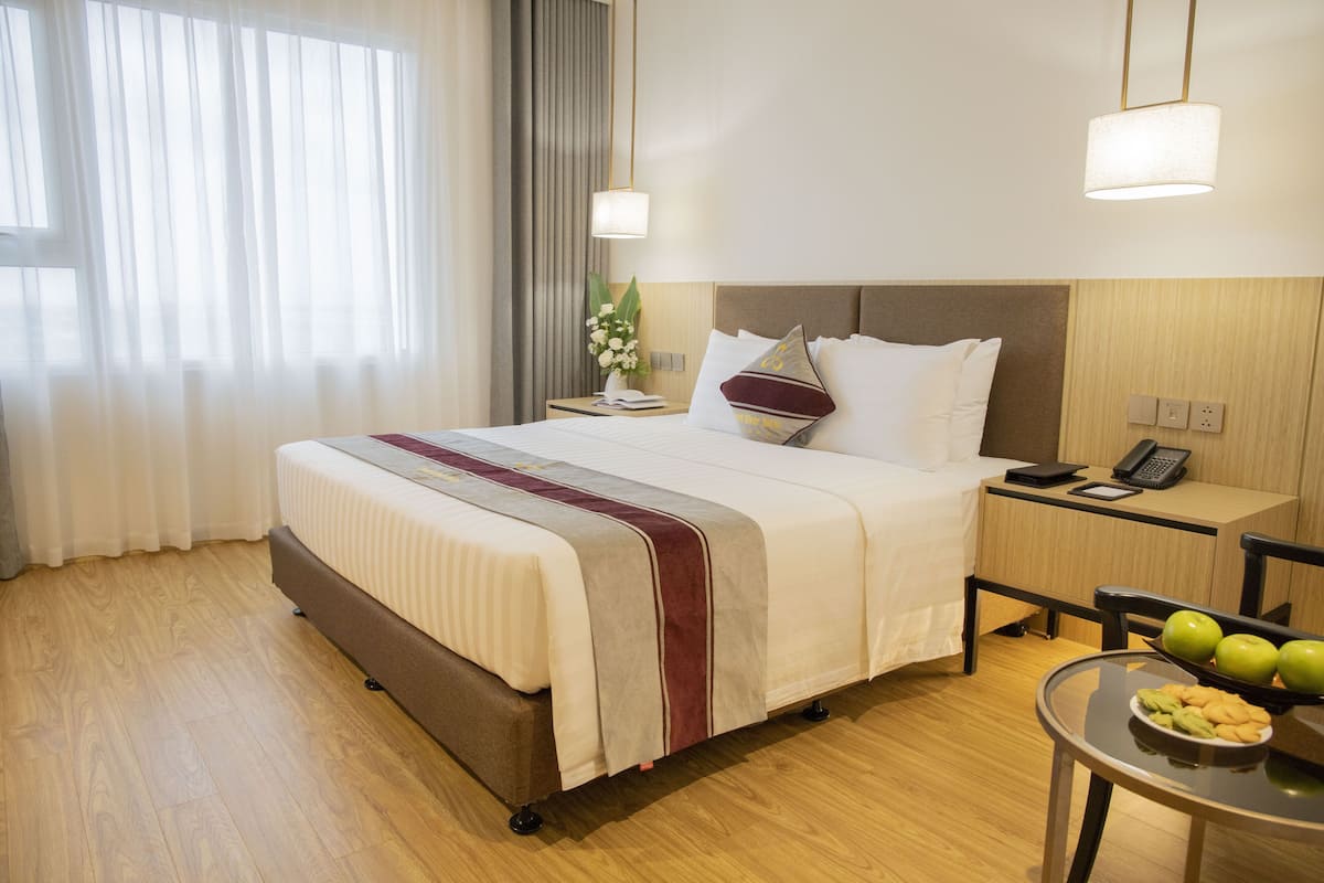 A hotel room with a large bed, bedside table, and a small table with apples.