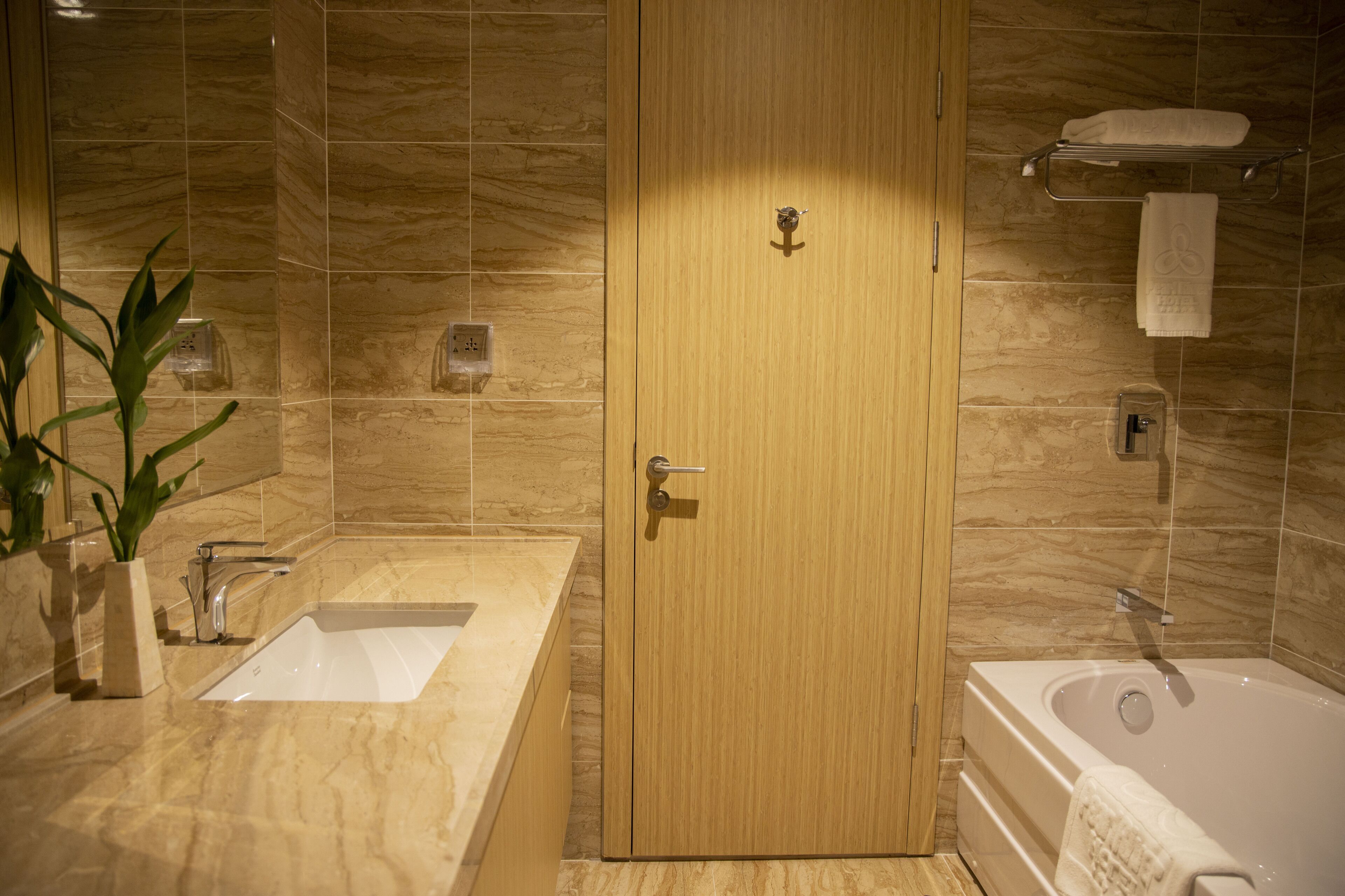 A modern bathroom with a wooden door, a sink, a bathtub, and a towel rack.