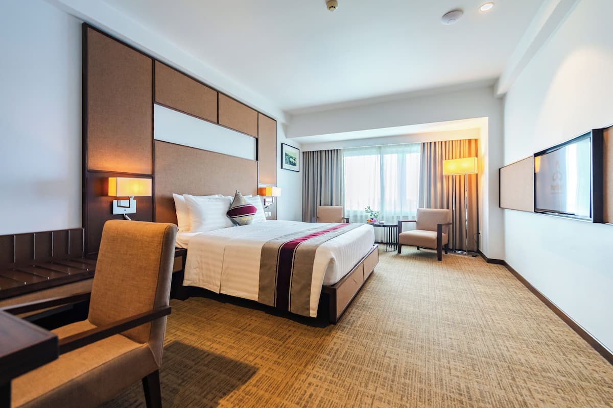 A hotel room with a large bed, a desk, a chair, a TV, and a window with curtains.