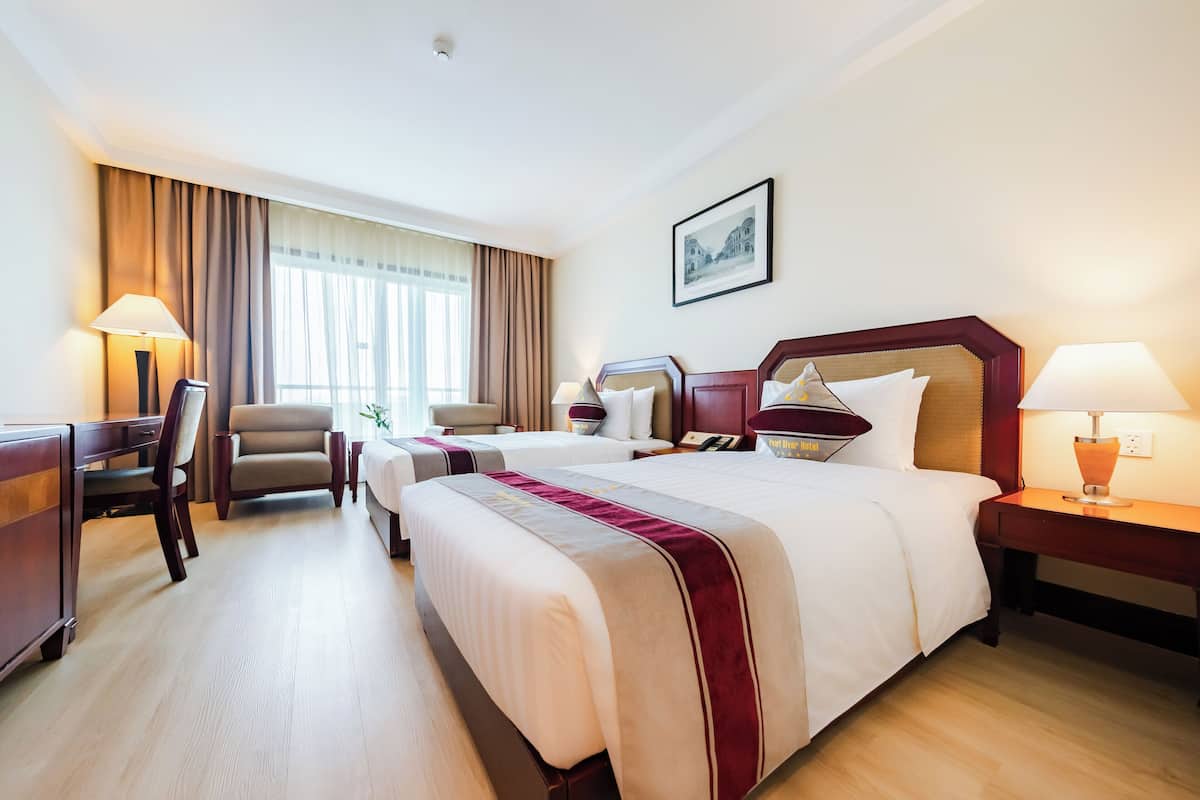 A hotel room with a large bed, two bedside tables, a desk, a chair, and a window with curtains.