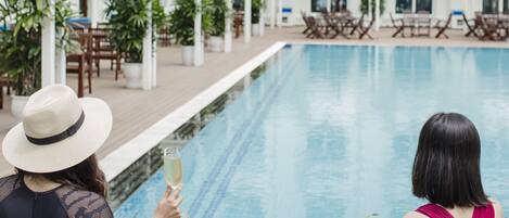 Zona de piscina con sillones de descanso, una piscina y un edificio con varios balcones.