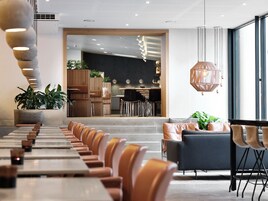 En moderne restaurant med lange borde og stole, et barområde og store vinduer.
