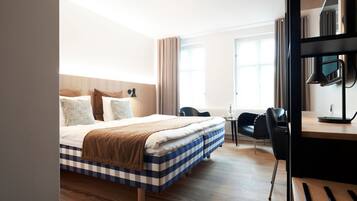 Habitación de hotel con una cama grande, un escritorio con lámpara, una silla y una ventana con cortinas.