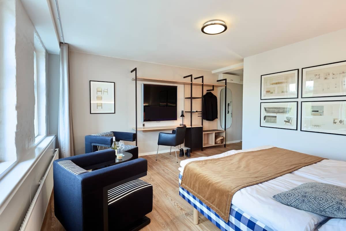 Une chambre d’hôtel moderne équipée d’un lit, d’un bureau, d’une chaise et d’une grande fenêtre.