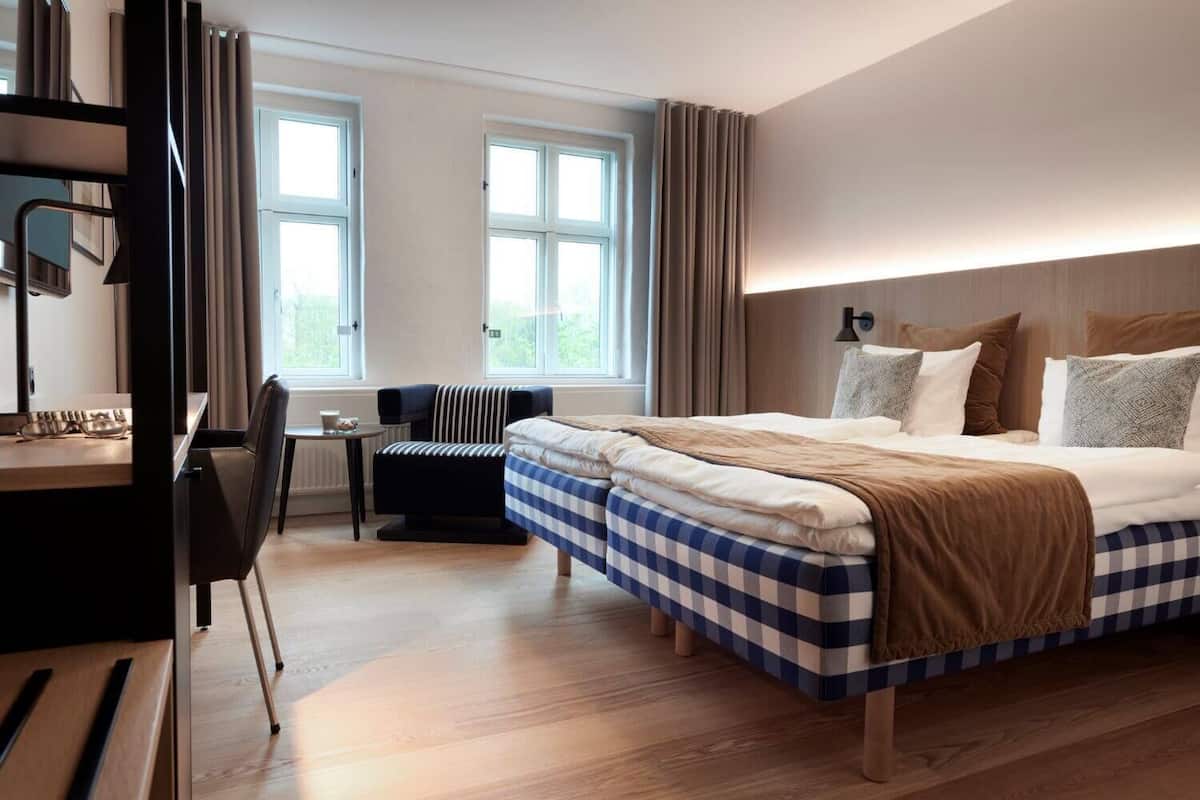 Une chambre d’hôtel avec un grand lit, un bureau avec une chaise et deux fenêtres.