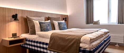 A modern bedroom with a checkered bedspread, a wooden headboard, bedside lamps, and a window with curtains.