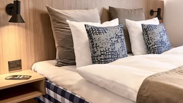 Uma cama bem arrumada com colcha xadrez, cabeceira de madeira e almofadas estampadas.