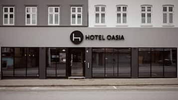 The exterior of Hotel Oasia, featuring a modern facade with large glass windows and a prominent logo above the entrance.