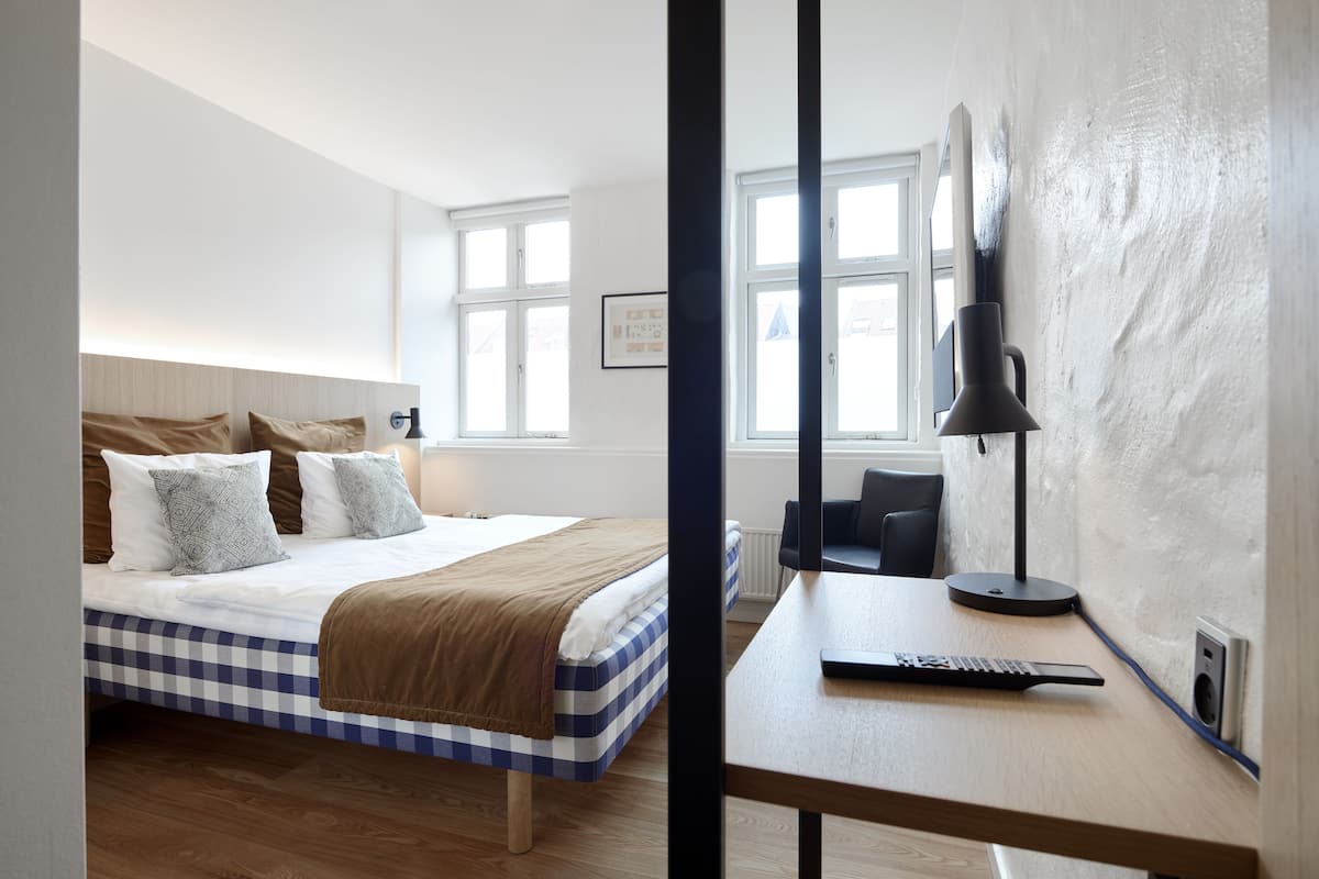 Une chambre d’hôtel avec une couvre-lit à carreaux, un bureau doté d’une télécommande et une grande fenêtre donnant sur un beau paysage.