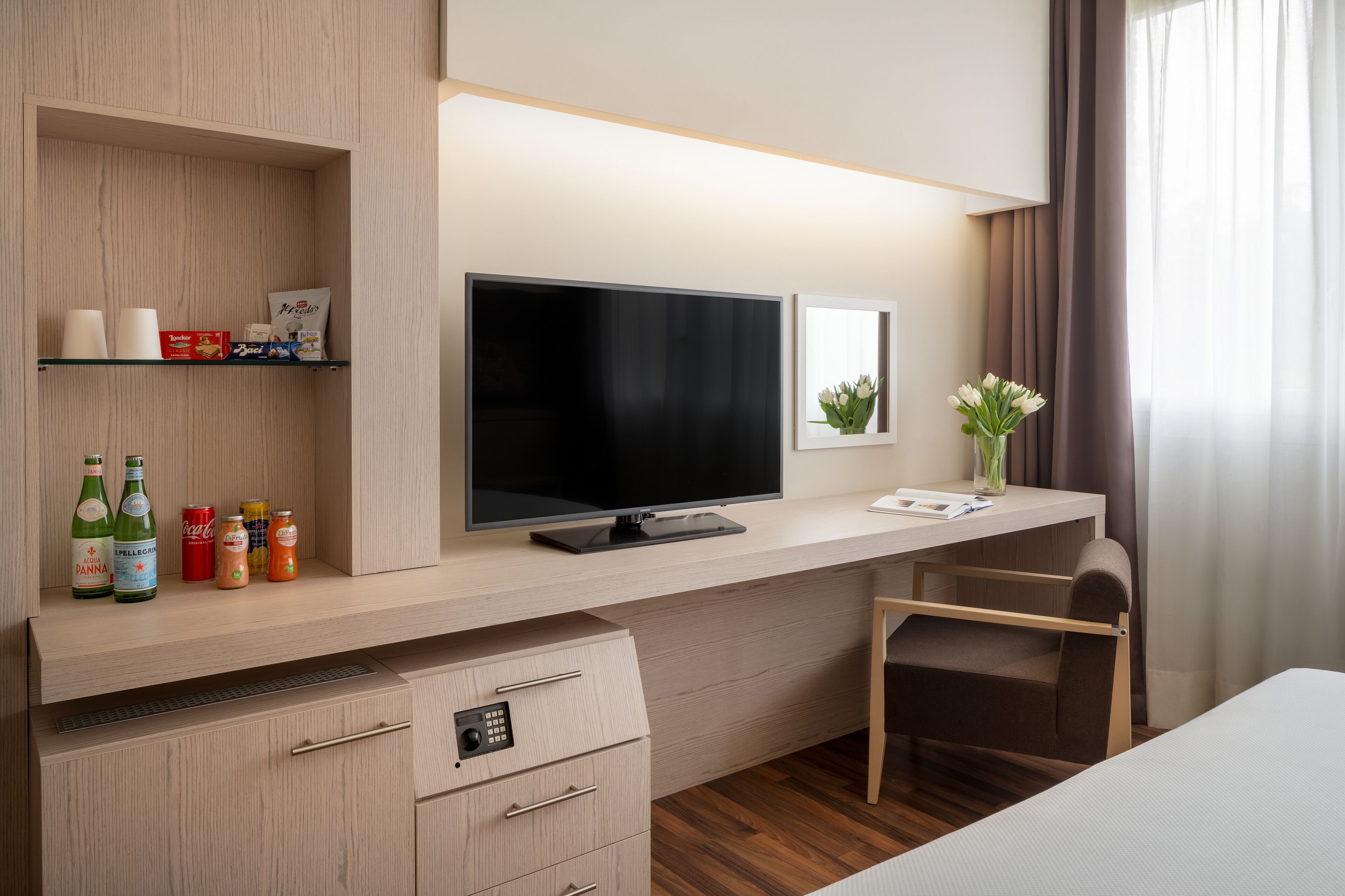 Habitación de hotel con escritorio de madera, televisor de pantalla plana, una silla, una cama y estante con bebidas.