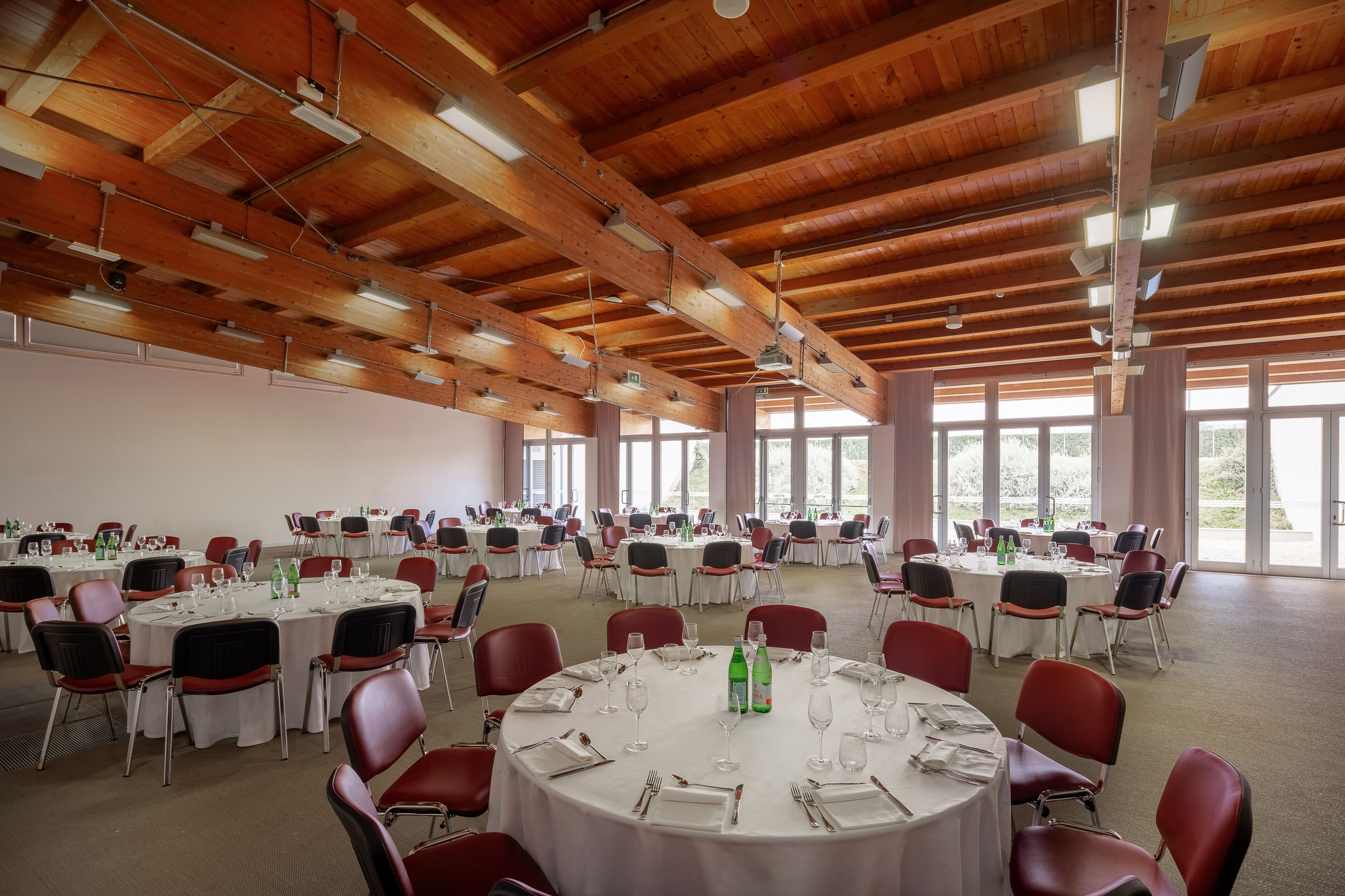 A large hall with round tables and red chairs, arranged for a formal event.