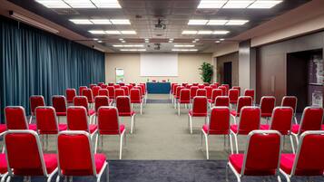 A conference room with rows of red chairs, a projector screen, and a presentation area.