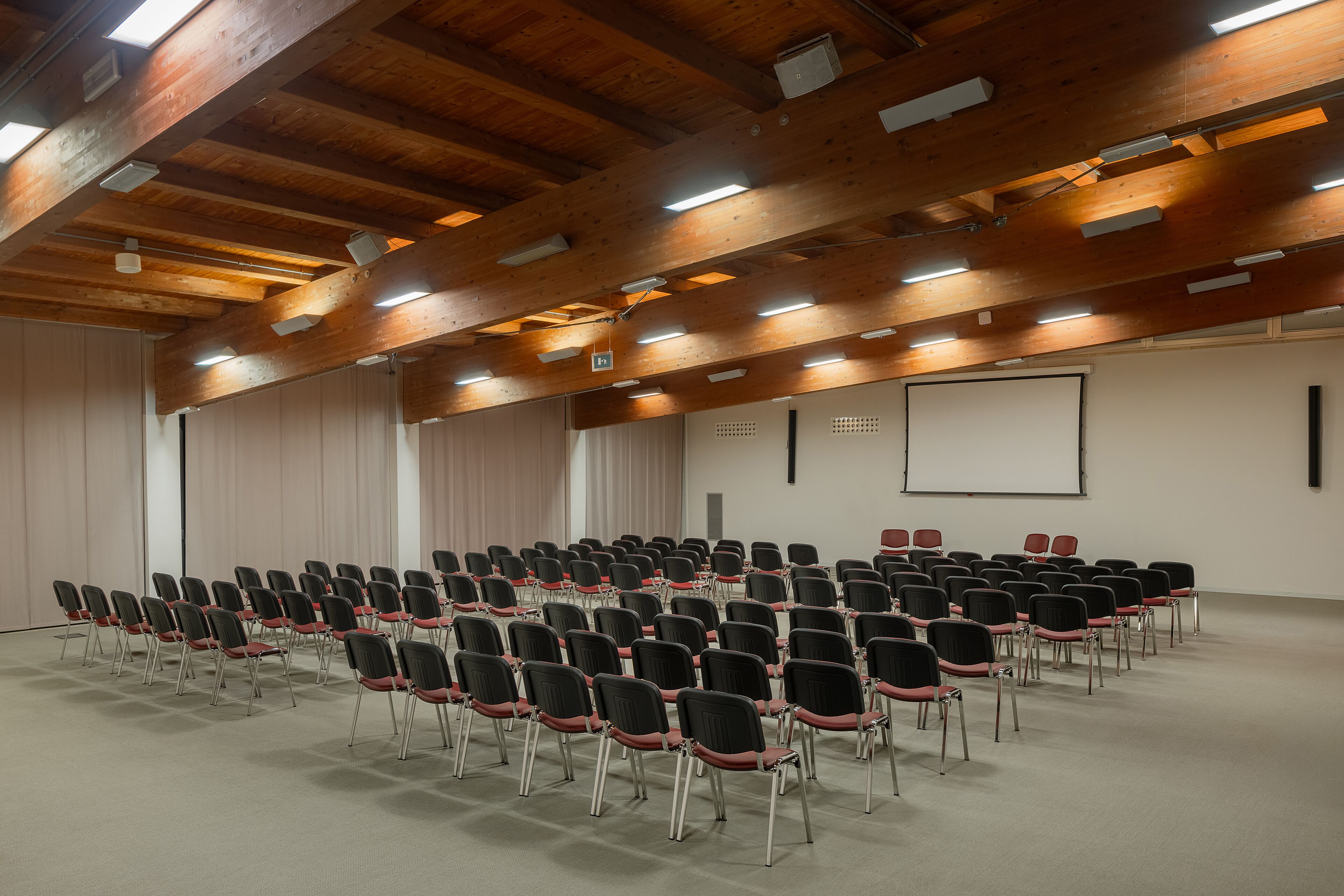 A conference room with rows of chairs, a projector screen, and wooden beams on the ceiling.