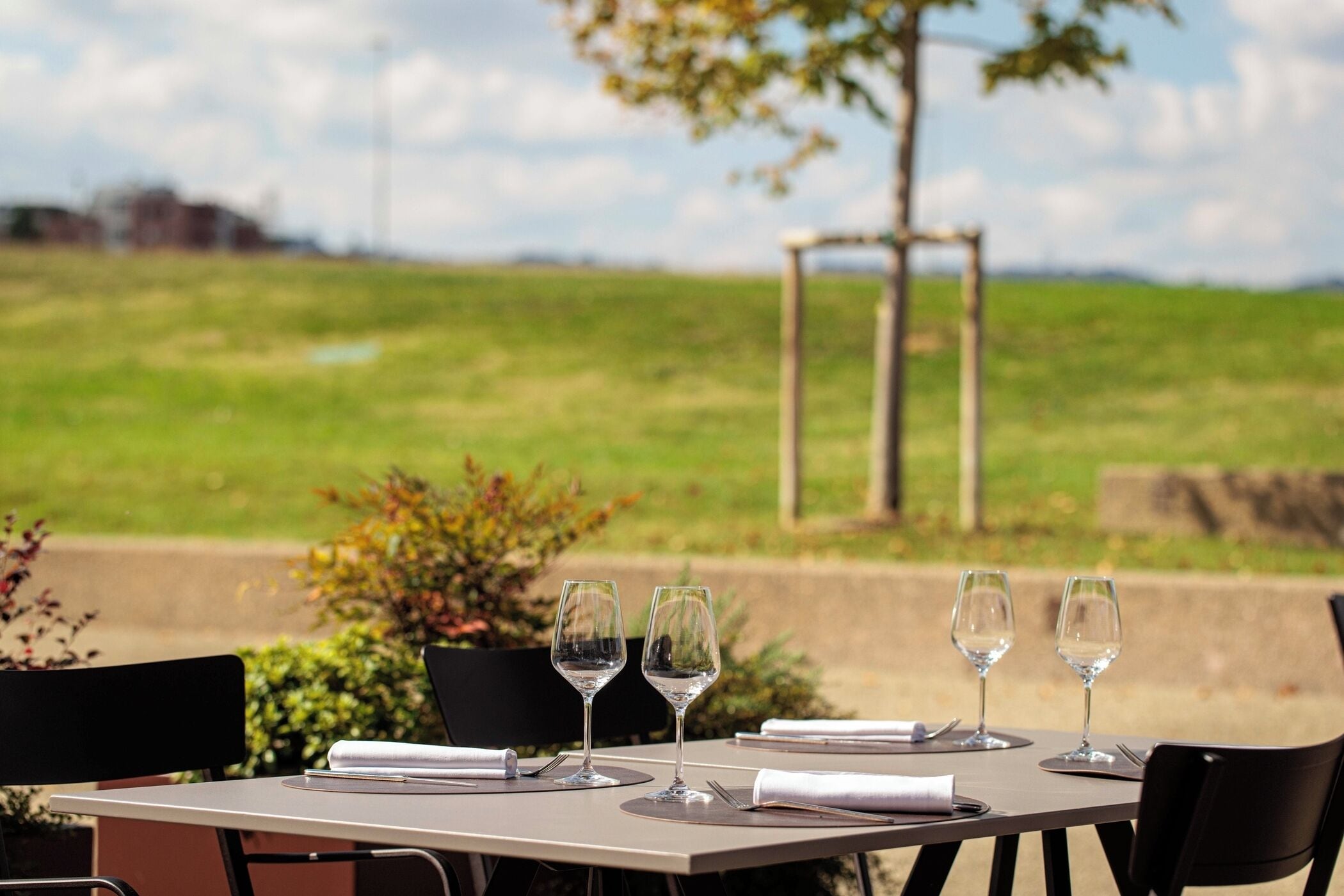 Een buitentafel met vier wijnglazen en een menukaart, met op de achtergrond een grasveld en een houten pergola.