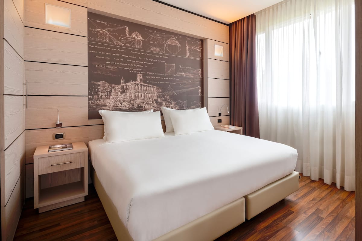 Ein modernes Hotelzimmer mit einem großen Bett, Holzboden, einem Nachttisch und einer Wandleuchte.