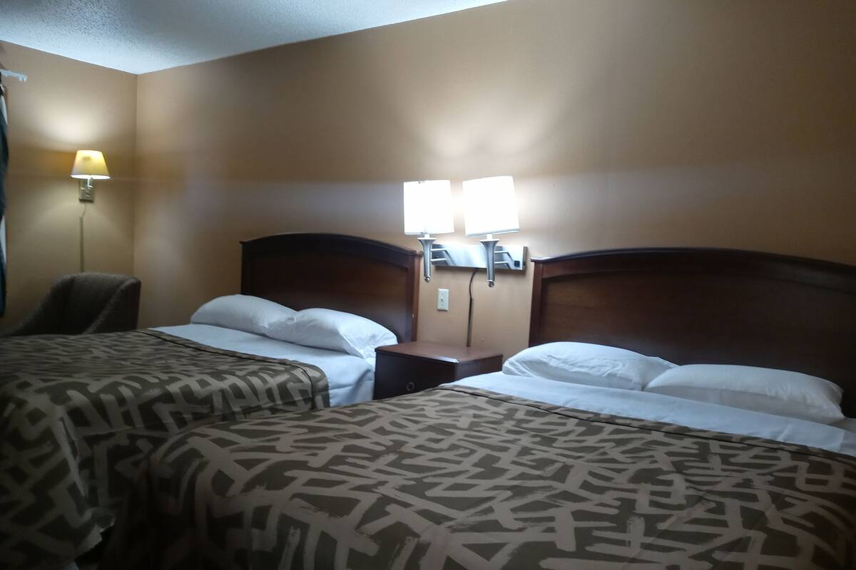 A hotel room with two beds, a nightstand, a lamp, and a chair.