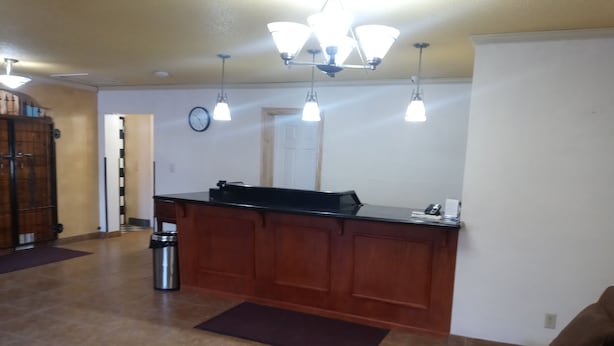 Una cucina con un piano di lavoro in marmo, mobili in legno e un'isola nera. Si notano luci a sospensione, un cestino della spazzatura e un orologio appeso al muro.
