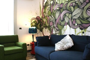 Una habitación con un sofá azul, un sillón verde y una pared con arte abstracto.