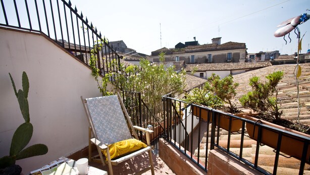 A balcony with a chair, a cactus, and a table with magazines. - Bad - Bed & Breakfast and Design (Catania)