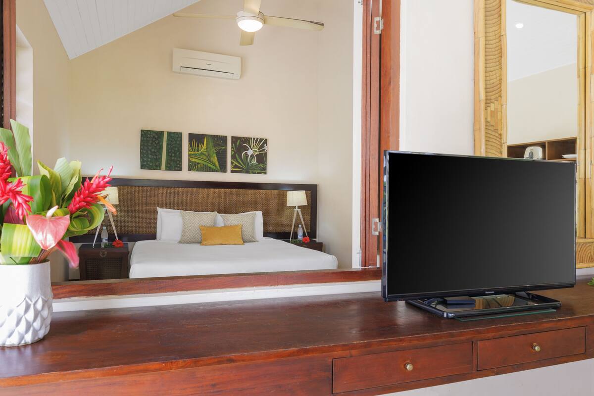 A hotel room with a bed, bedside table, TV, and a large mirror.