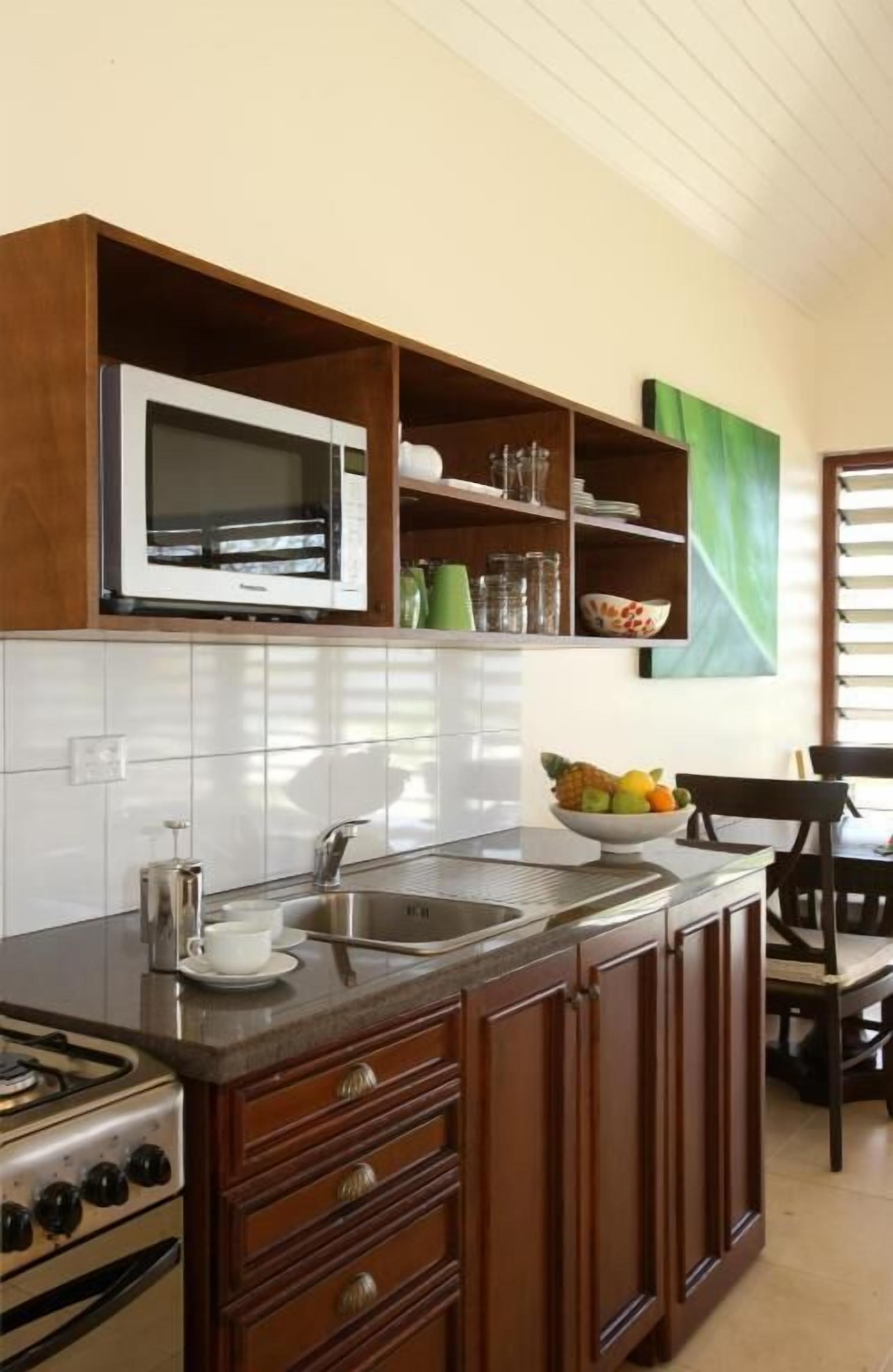 Una cocina con microondas, pileta, estufa, alacenas de madera y un frutero.