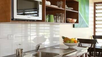 Una cocina con microondas, pileta, estufa, alacenas de madera y un frutero.
