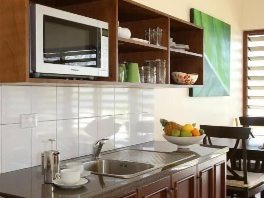 Una cocina con microondas, pileta, estufa, alacenas de madera y un frutero.