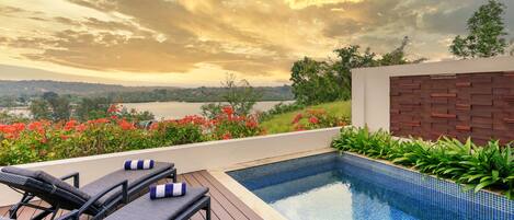 A poolside area with lounge chairs and a view of a lake at sunset.
