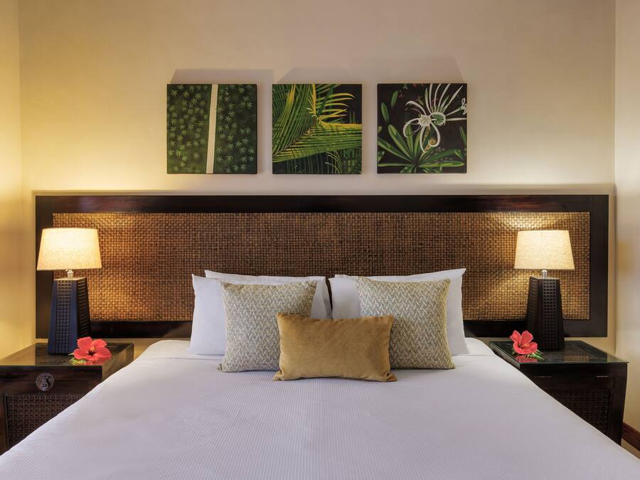 A hotel room with a large bed, two nightstands, two lamps, and three wall-mounted artworks.