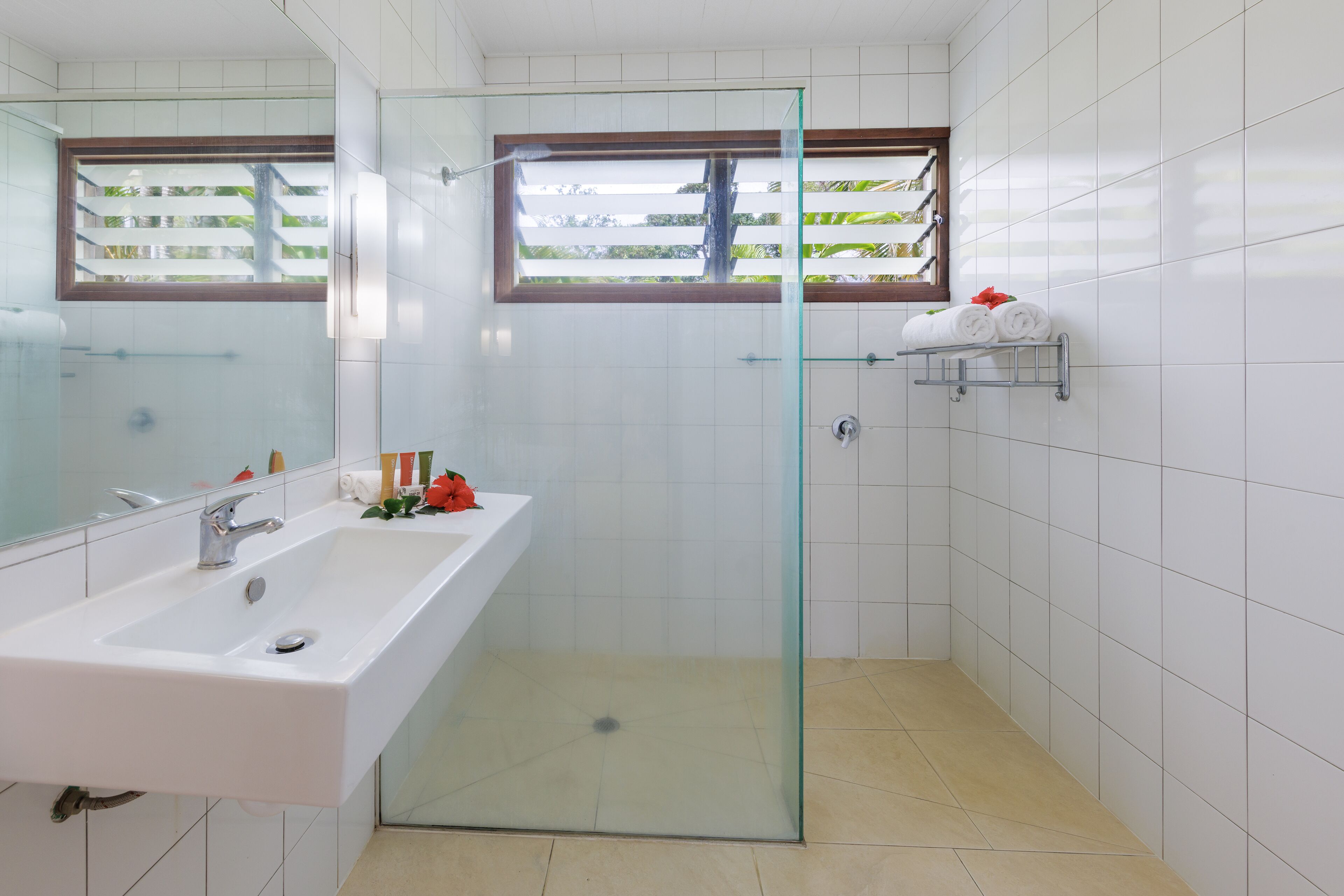 Un baño moderno con cabina de ducha de vidrio, un lavabo blanco y una ventana con vistas a zonas verdes.