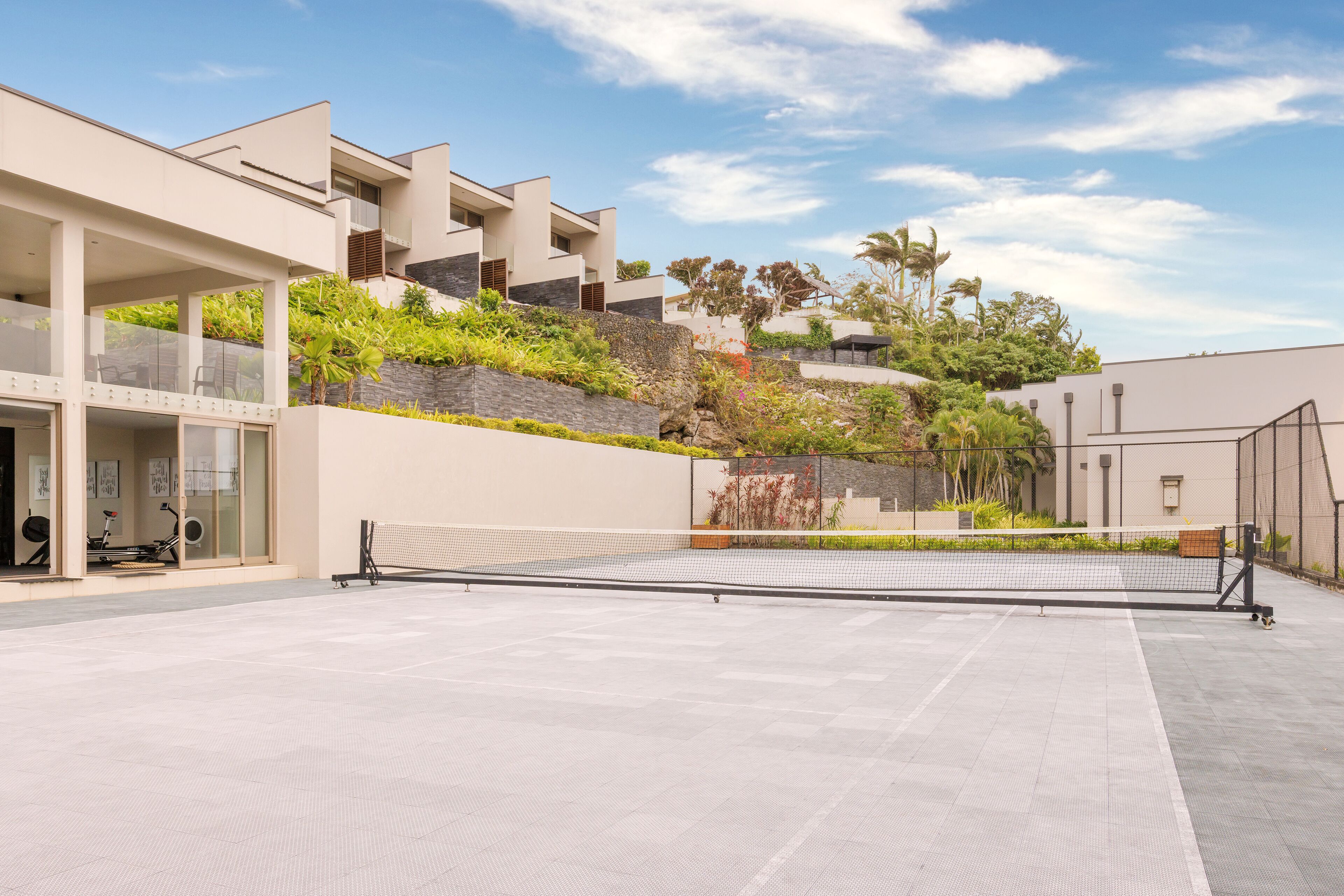 A modern building with a tennis court, outdoor seating, and a landscaped garden.