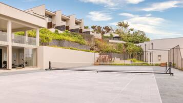 A modern building with a tennis court, outdoor seating, and a landscaped garden.