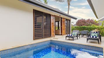 Una piscina con borde de azulejos, junto a un edificio con ventanas amplias y puertas corredizas.